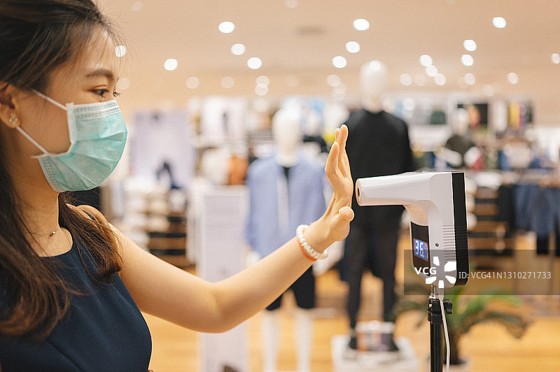 侧视图新冠肺炎疫情期间，一名亚洲华人女性戴着口罩检查百货商店出售的服装图片素材