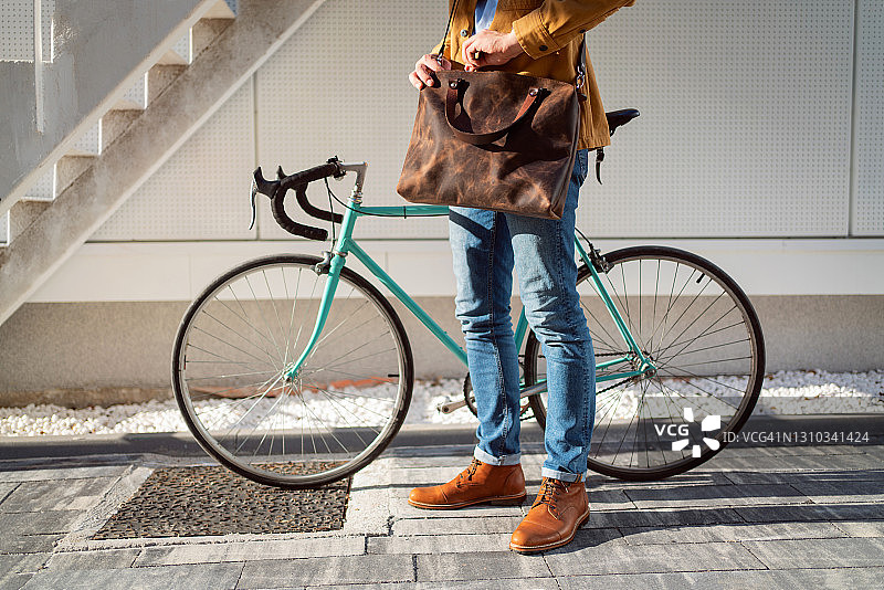 一个面目全非的人站在他的自行车旁边，同时关闭他的皮包图片素材