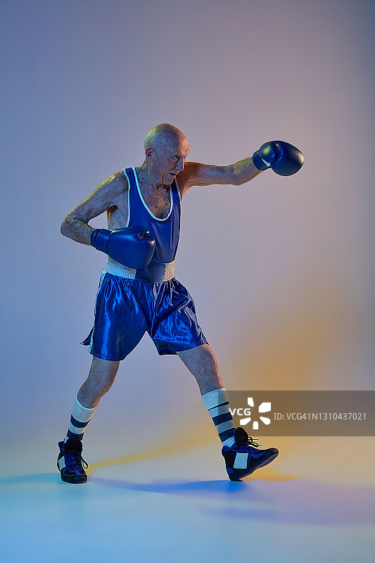 资深男子穿着运动服拳击孤立在梯度演播室背景下霓虹灯。运动、活动、运动、幸福的概念。Copyspace,广告。图片素材