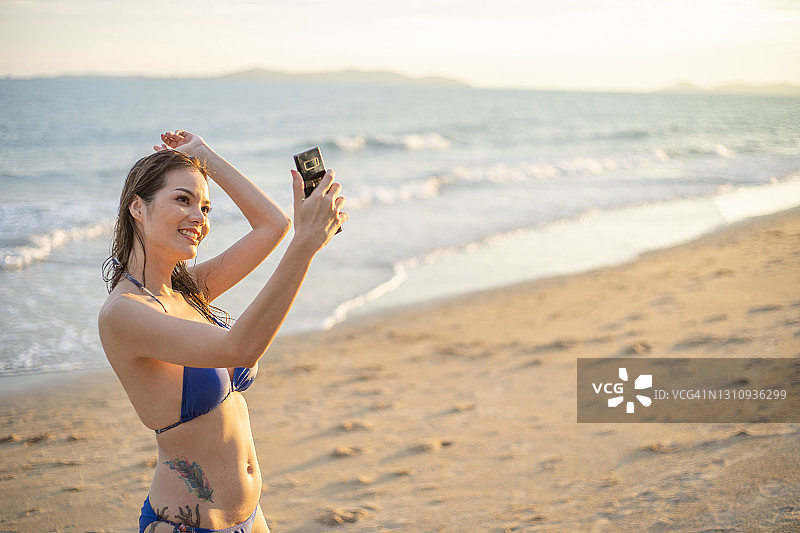 年轻女性在海滩上自拍和用比基尼打视频电话。图片素材