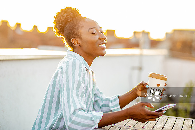年轻的非洲裔美国妇女享受在屋顶上日落和喝咖啡图片素材