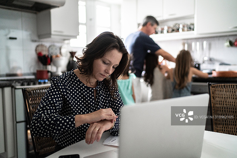 成熟的女性在家里和家人一起检查时间和使用笔记本电脑图片素材