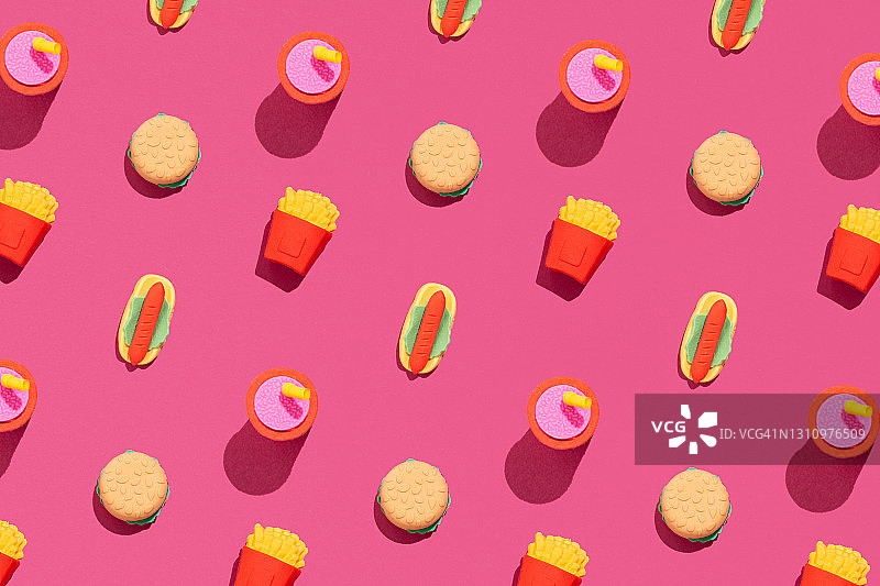 热狗，汉堡，薯条和可乐的快餐图案在大胆的粉红色背景。极简垃圾食品平面摆放的想法。图片素材