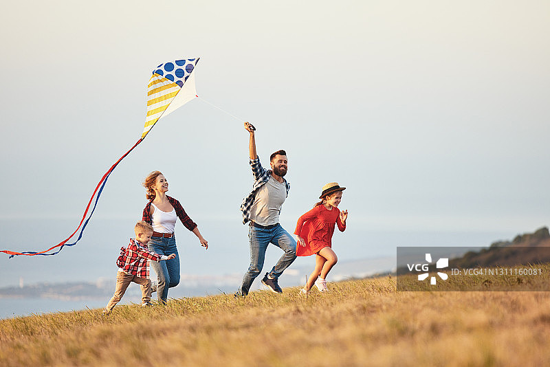 幸福的家庭，爸爸妈妈和孩子们在日落时分在大自然中放风筝图片素材