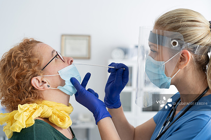 医生戴上防护面罩，从一名妇女身上提取鼻拭子，以检测是否可能感染冠状病毒图片素材