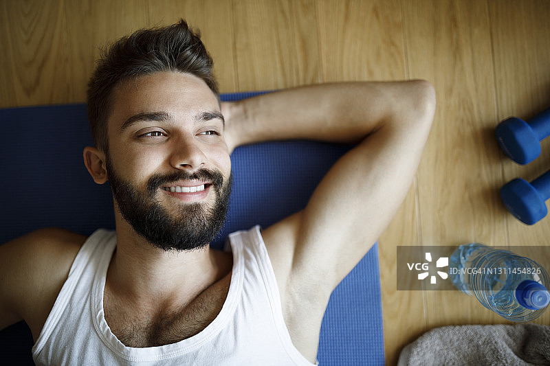 一个微笑的年轻人在家锻炼后放松图片素材
