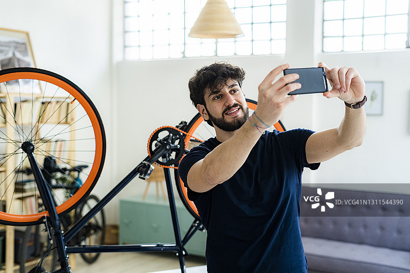年轻人站在家里翻倒的自行车旁用智能手机自拍图片素材