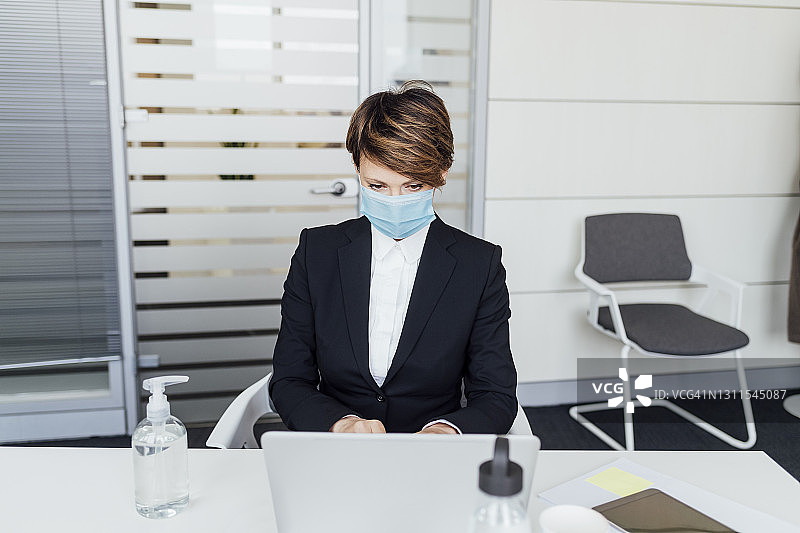 女商人戴着防护面罩在办公室用笔记本电脑工作图片素材