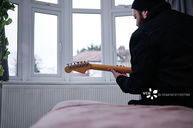 一个成熟的男人坐在家里的床上弹吉他图片素材