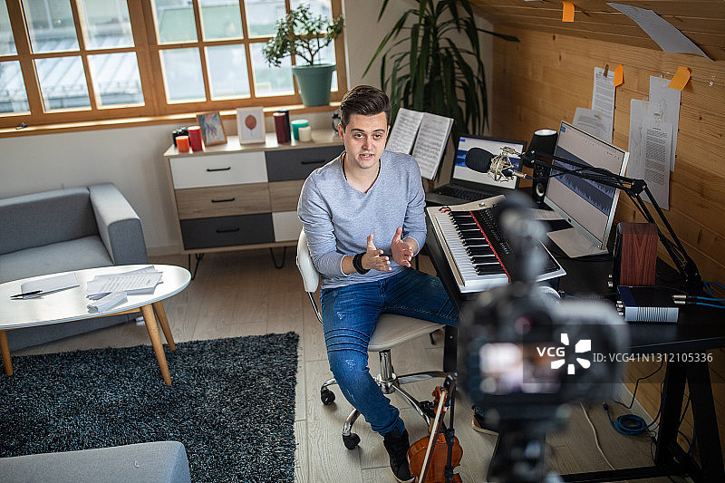 年轻的音乐家坐在椅子上，在他家里的录音棚录制视频博客图片素材