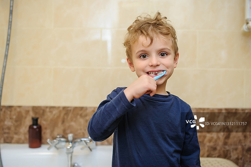 一张穿着蓝色t恤的金发男孩在浴室里刷牙的照片图片素材