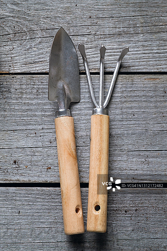 园艺工具，一个小铲子，一个耙子。在木桌的背景上种植和播种鲜花、植物或蔬菜。种植有机农产品。空间的副本。图片素材