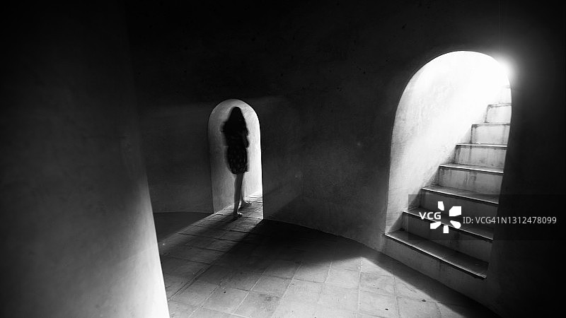 一个不知名的女性独自走在黑暗古老的地下室里。图片素材