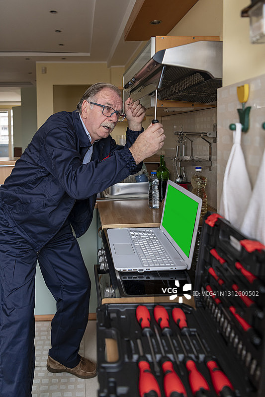 一位年长的维护工程师正在厨房里工作，修理排气扇。图片素材
