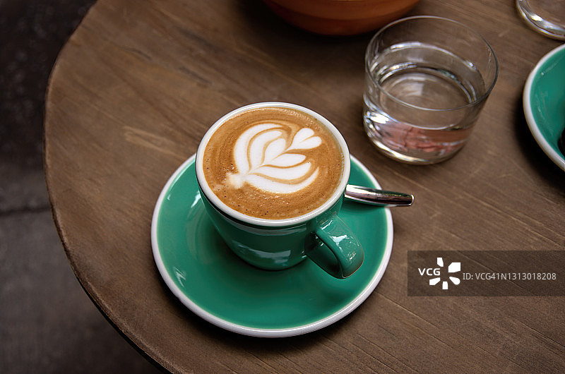 一杯白咖啡装在绿白相间的杯子和水杯里，放在户外咖啡馆的一张木桌上图片素材