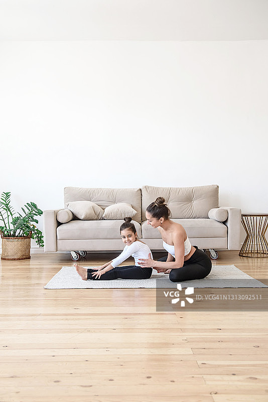 母亲和女儿一起在家里的地毯上做运动练习瑜伽伸展图片素材