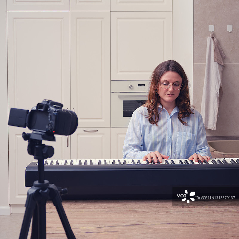 一个穿着蓝色衬衫的女人用摄像机录下钢琴课。在家庭厨房里学习音乐图片素材