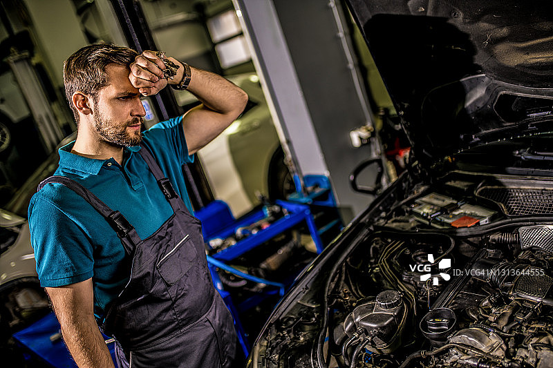 担心的机修工在汽车修理厂检查发动机问题。图片素材