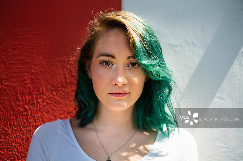 在白色和红色的背景下，墨西哥城的一位绿色头发的年轻女子看着摄像机图片素材
