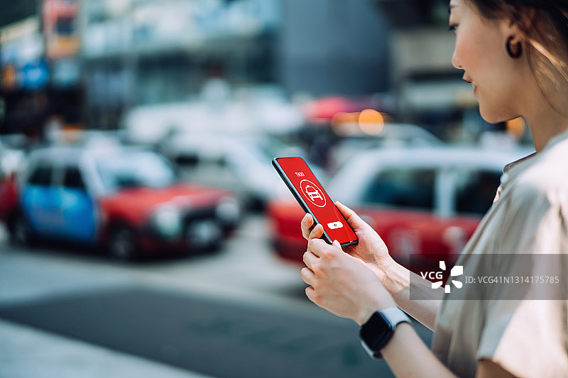 一名年轻的亚洲女子用智能手机上的移动应用订车，在市中心的街道上等待出租车。日常生活中的科技和交通图片素材