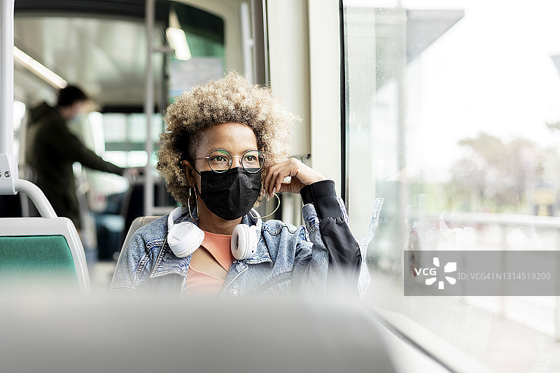 一名妇女戴着面具在有轨电车中透过窗户看图片素材