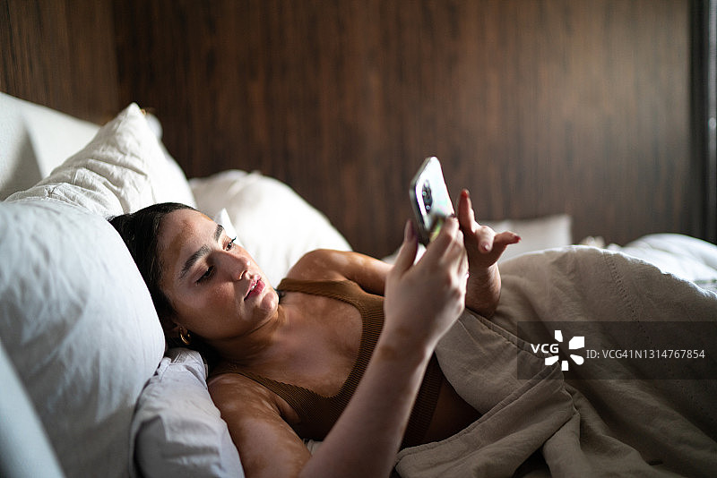 年轻女子在床上用智能手机在家图片素材