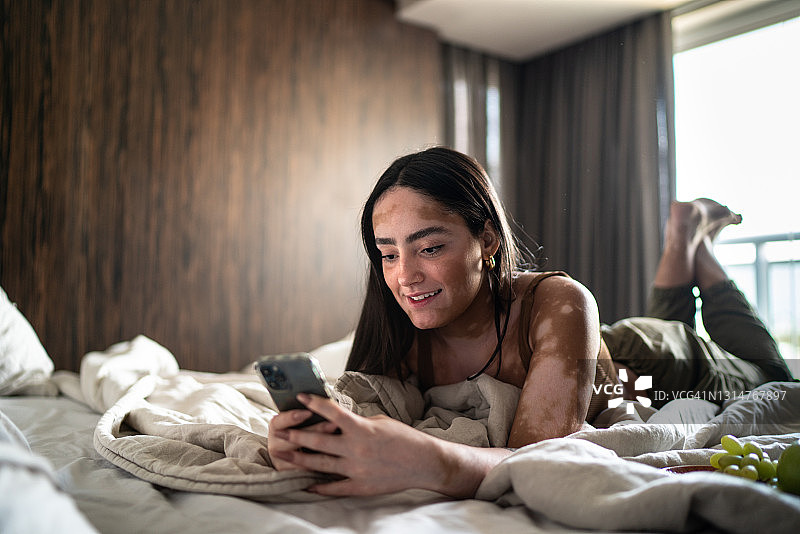 年轻女子在床上用智能手机在家图片素材