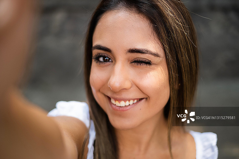 年轻的西班牙女子微笑着，眨眼，在墨西哥城自拍，手机的视角图片素材