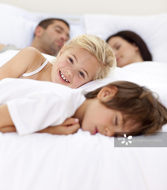 小女孩在床上微笑，而她的家人都在睡觉图片素材