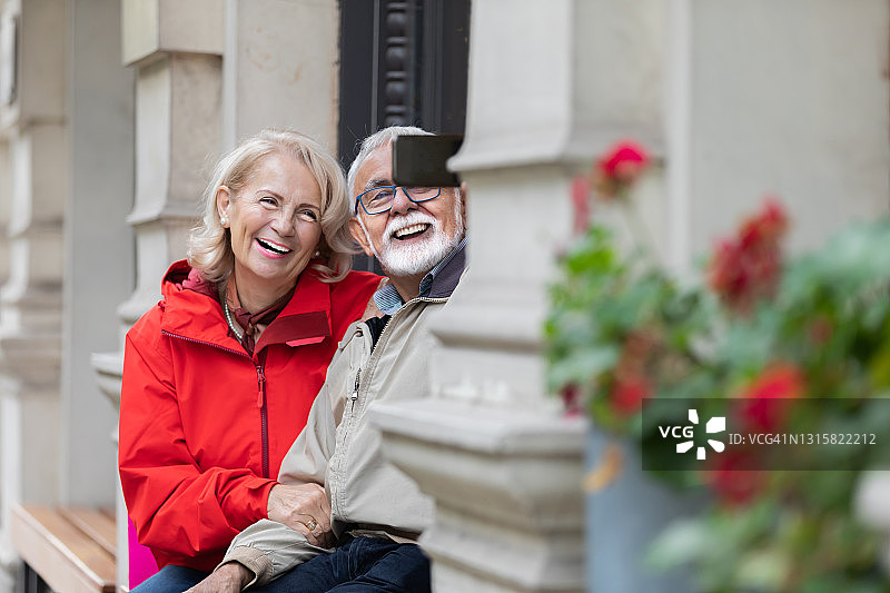 一个快乐的老夫妇在爱谁坐在公园和拍照自己的肖像。图片素材