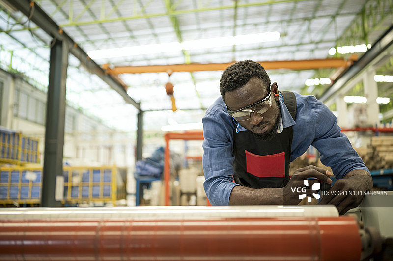 非裔美国人维护工程师在工厂使用工具调整塑料挤出吹膜机。生产过程中的预防性维护。图片素材