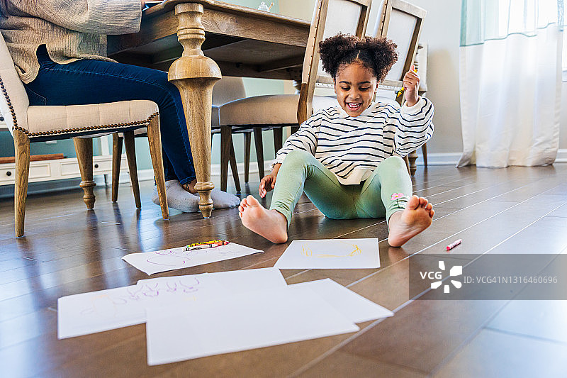 快乐的女孩坐在家里的硬木地板上在纸上画画图片素材