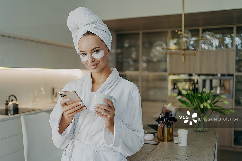 幸福的女人在浴衣和毛巾在头上放松与一杯茶，同时做美容程序在家里图片素材