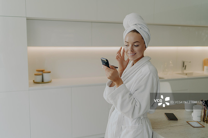 快乐健康的女人在浴袍上应用护肤产品后，淋浴或沐浴在家图片素材