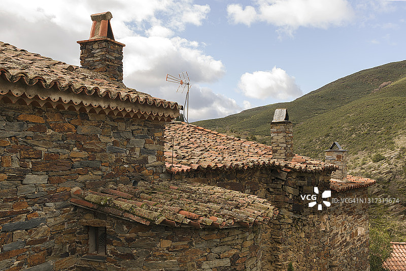 质朴的石头和石板立面，有瓦片屋顶和烟囱。图片素材