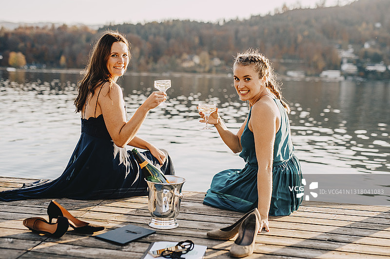 面带微笑的女性活动策划人坐在湖边的码头上，手里拿着香槟图片素材