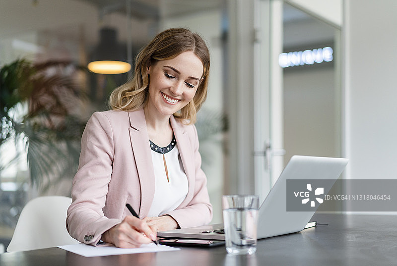 微笑的女企业家在桌上用笔记本电脑写文件图片素材