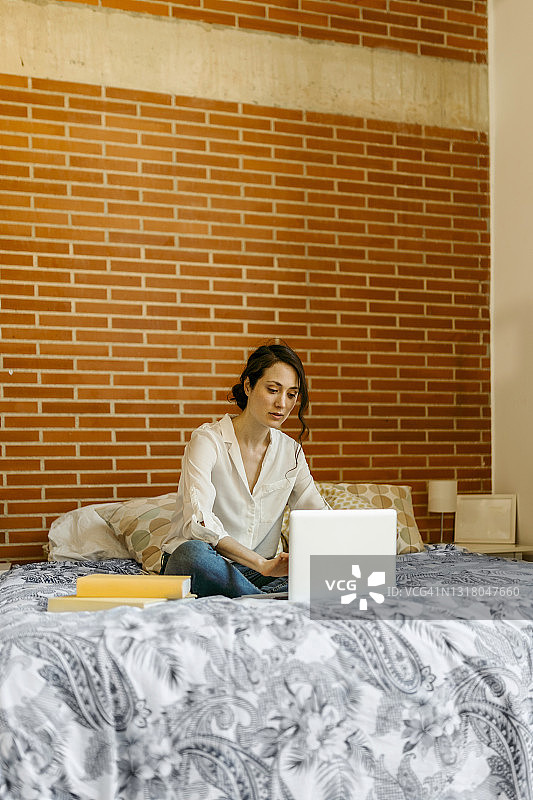 坐在家里床上使用笔记本电脑的女人图片素材