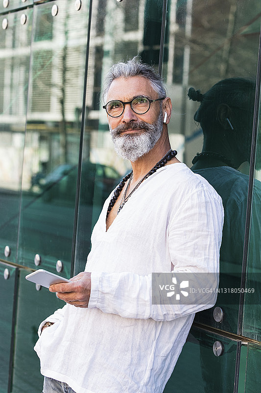 胡子男人靠在玻璃墙上玩手机做白日梦图片素材