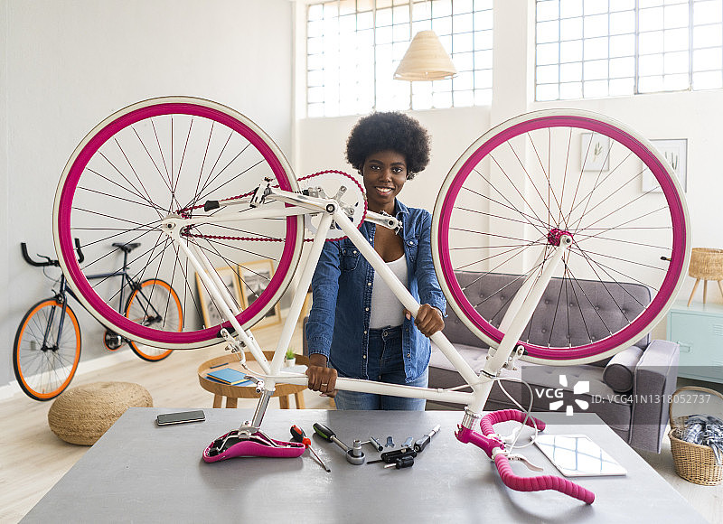 微笑的年轻女子拿着自行车在桌子上，而修理在家里图片素材