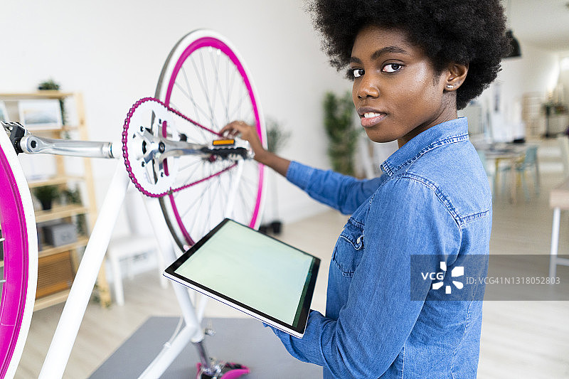 年轻女子用数字平板电脑在家修理自行车图片素材