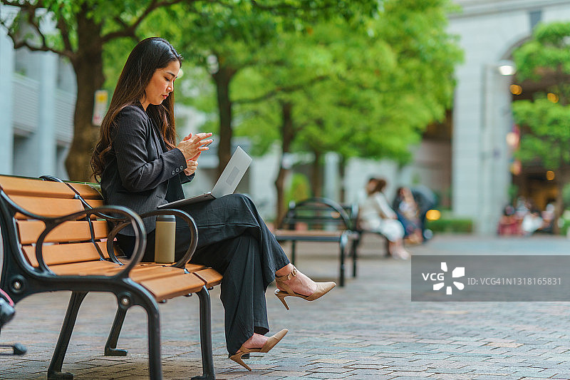 美丽的女商人坐在长椅上放松和使用电话在城市图片素材