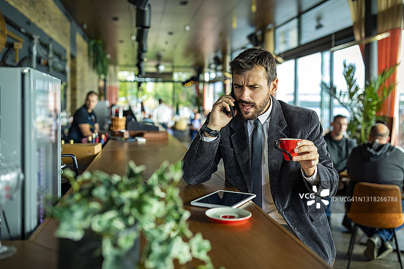 穿着得体的年轻商人正在Café享受热饮，并在他的电话不愉快的对话中制定一些严肃的商业计划。图片素材