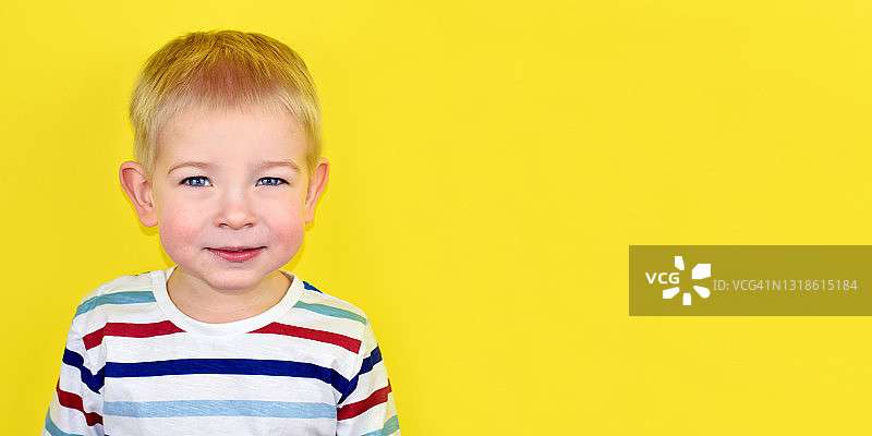 彩色背景上的快乐微笑的小男孩。黄色背景上的美丽的两岁欧洲男孩的肖像。为文本复制空间。图片素材