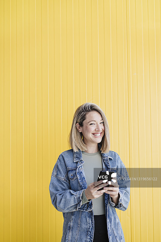 微笑的女人拿着手机站在墙前图片素材