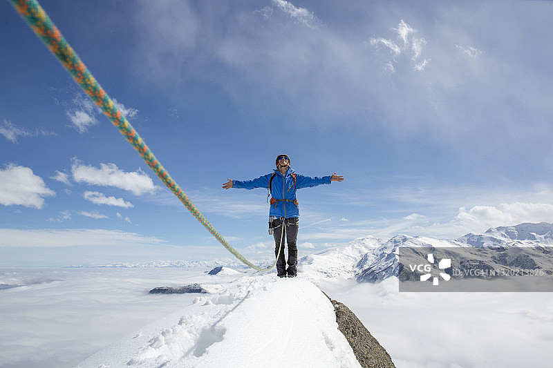 登山者站在积雪的山顶上，用绳子和手臂伸展图片素材