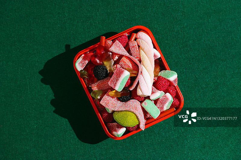 俯视图的红色塑料盒充满橡皮糖在一个绿色的背景。图片素材
