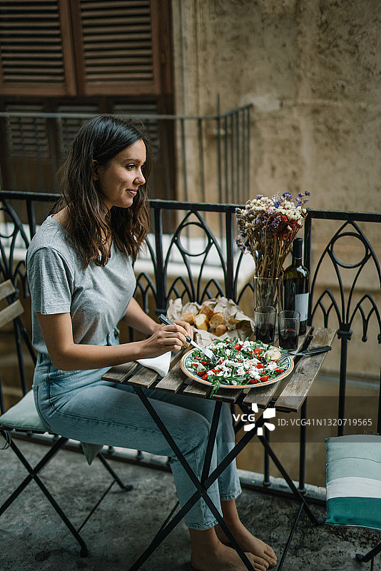 一位年轻女子在她的阳台上享用一顿有沙拉和葡萄酒的午餐图片素材