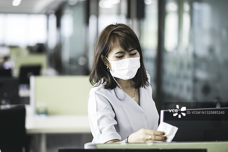 COVID-19大流行期间，在办公室使用消毒剂消毒监测仪表面的妇女图片素材