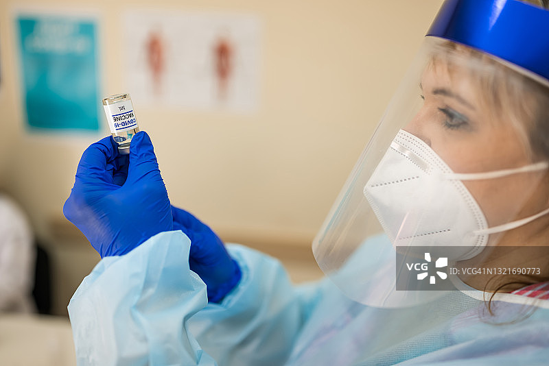身穿个人防护服的女医护人员正在将COVID-19疫苗瓶中的液体注入注射器图片素材